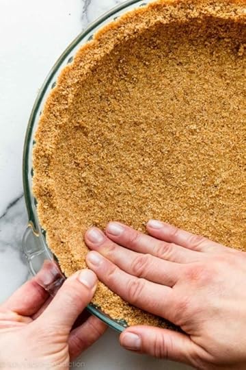 two hands pressing graham cracker crust into glass pie dish.
