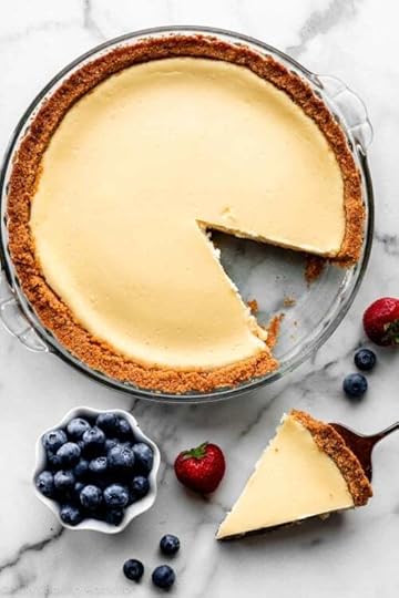 cheesecake pie in glass pan with slice taken out and blueberries and strawberries scattered next to the dish.