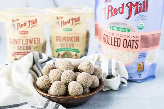 small wood bowl of energy balls with opened bags of oats, sunflower seeds and pumpkin seeds in the background