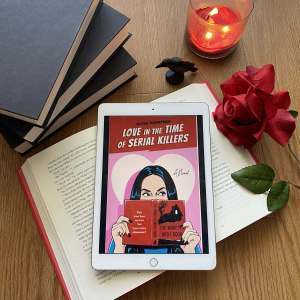 Book cover surrounded by a stack of books, a red candle, a red rose, and a black raven figurine