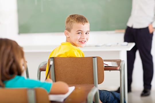 A boy around eleven years old sits at a desk in a classroom and turns to smile at the camera. Positivity and growth are a result of celebrating the wins, or seeing how far you've come.