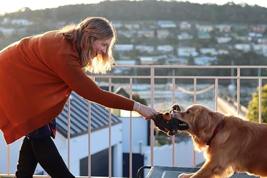 A white woman with blonde hair playing tug of war with a golden retriever dog.