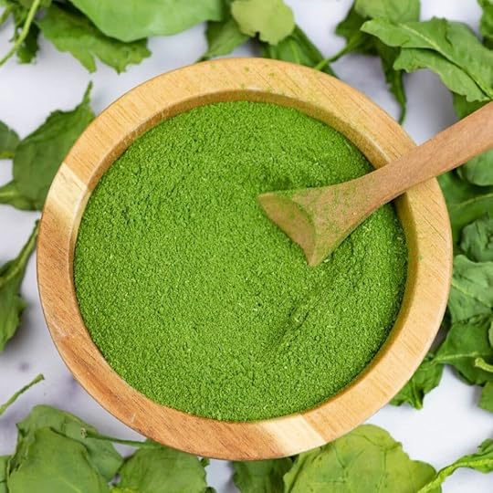 Overhead image looking down into a small wooden bowl filled with spinach powder.