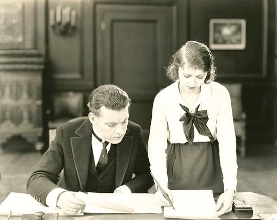 Black/white photo of man and woman working together on papers in an office, early 20th century