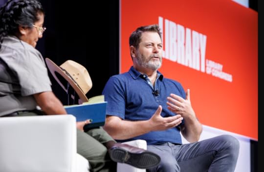 Nick Offerman, seated, wearing a blue knit pullover, speaks to NPS ranger ?? , in uniform, on the NBF main stage.