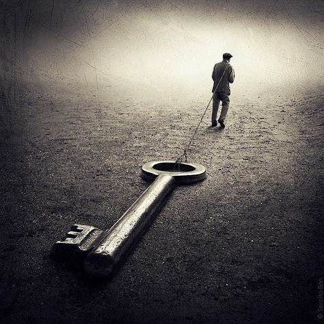 A black and white image of a man walking in a barren empty, desert-like land, his back to the camera dressed in suit and flat cap, holding onto a rope over his shoulder, dragging an giant metal old key, with a round looped top. Created by Sarolta Ban.