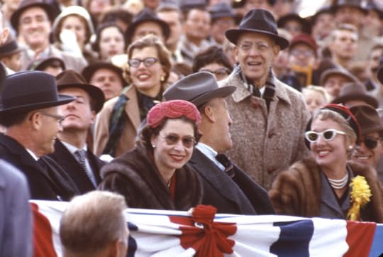 Queen Elizbeth II in a crowd, smiling wearing a pink hat and sunglasses