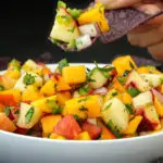 mango peach salsa on a blue corn tortilla chip over a bowl of salsa.