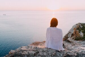 woman sitting on rocks looking at water, guilt, shame, breaking free