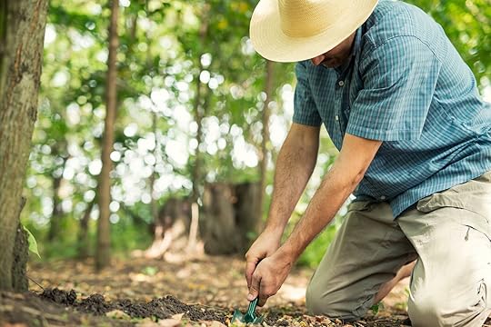 man in sun hat digging a hole in the ground with trowel - how to poop in the woods