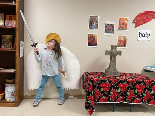 child holds up foam sword in front of angel wings and halo