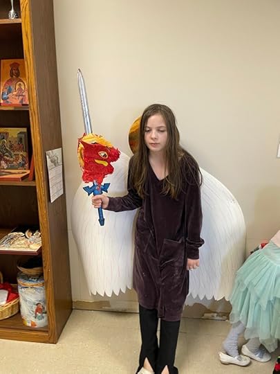 child holds up dragon pinata head on toy sword in front of angel wings and halo