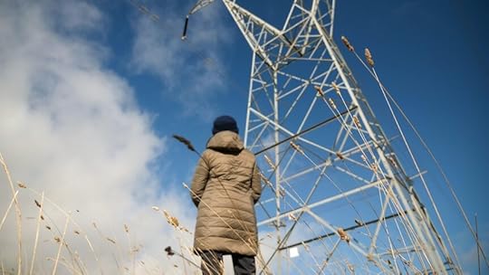 A woman looks up at a large transmission tower.