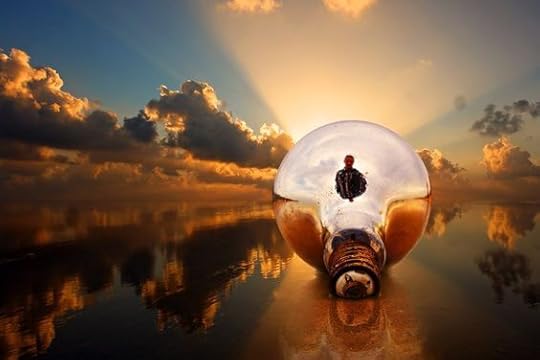 A picture of the back of a spotlight bulb lying on a wet sand beach. The sun is setting and the horizon shows lots of clouds against a blue sky, which are reflected in the surface of the sand. A beam of light is coming out of the lightbulb towards the setting sun. Created by Hermin Abramovitch