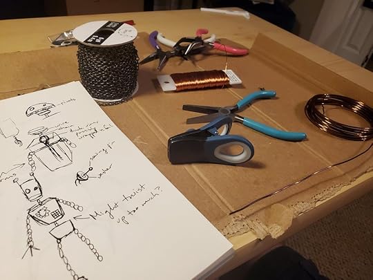 Work table with a drawing of a robot design, a spool of jewelry chain, a bag clip,