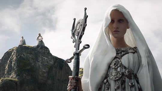 A pale hooded figure in white stands with a staff on The Rings of Power