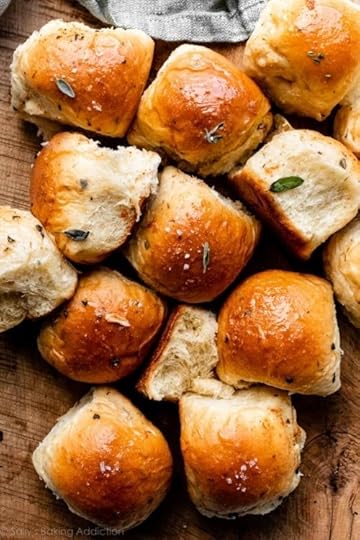dinner rolls garnished with fresh chopped sage on wooden cutting board.
