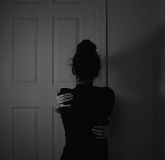 A black and white image of a women holding herself in her arms signifying strength in comforting self.