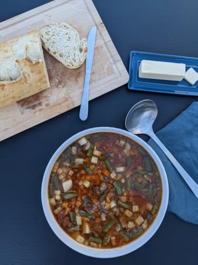 Vegetable Beef Soup on a black background with sourdough break on a cutting board with a butter knife, butter, and a ladle