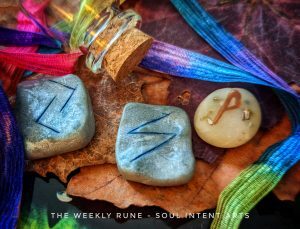 Elder Futhark runes Wunjo, Sowilo, and Jera with a small empty glass vial and a satin rainbow ribbon on a background of fall leaves and a green cat's eye
