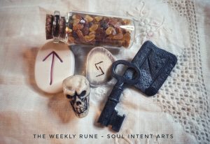 Elder Futhark runes Hagalaz carved into a wrought iron tile, Jera carved into a reindeer antler slice, and Tiwaz carved into a ceramic tile, with a small glass vial of Baltic amber chips, an antique iron key, and a small plastic skull on a cream-colored linen background