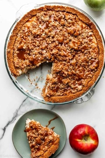 apple pie cheesecake topped with caramel sauce with 1 slice missing that's placed on green plate.