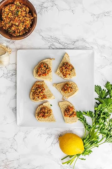 Sun-dried tomato green olive tapenade on small slices of bread on plate with fresh parsley, lemon, and bowl of tapenade on side
