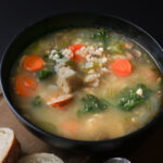 close up of turkey and rice soup in black bowl on a wooden board.
