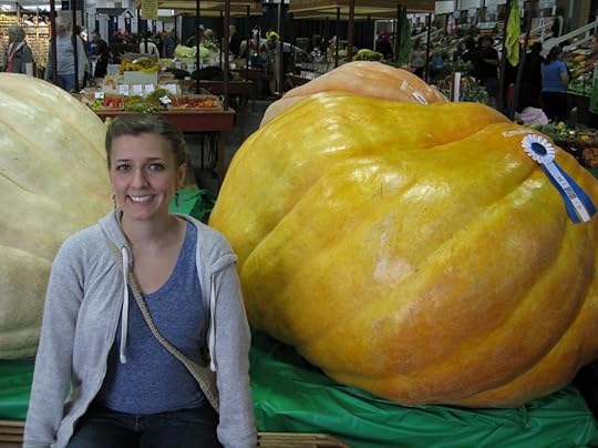 Photo of the author sitting in front of a giant pumpkin that is as big as she is (it has a ribbon it, from a fair).