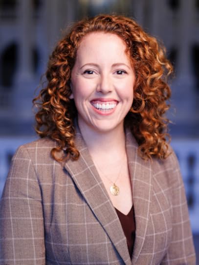 Katie Klenkel, smiling in a color portrait photo, wearding a suit coat.