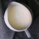 white sauce in white gravy boat on a gray cloth.