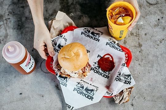 A hand holding a red tray with a sandwich on it and a drink in a yellow cup at Peg Leg Porker