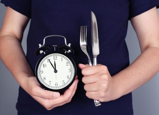 Hands holding alarm clock with fork and knife.