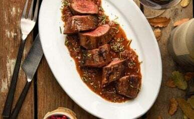 Pan seared venison tenderloin with a red wine sauce on a platter, alongside lingonberries and wild rice.