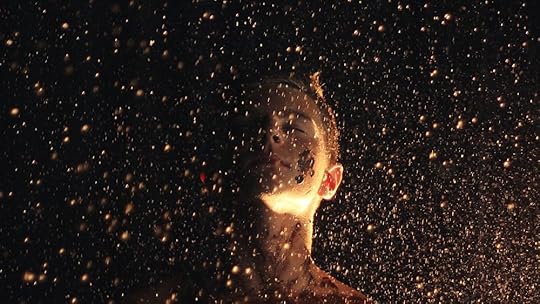 A smudged boy standing in the sparks rising from the fire with his eyes closed.