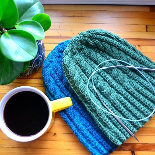 Green & Blue Trailfinder hats with circular needle and yellow coffee mug next to a plant