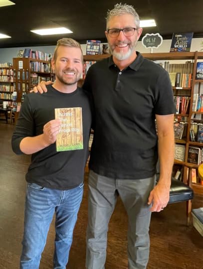 Two men, both in back t-shirts, holding up a book.