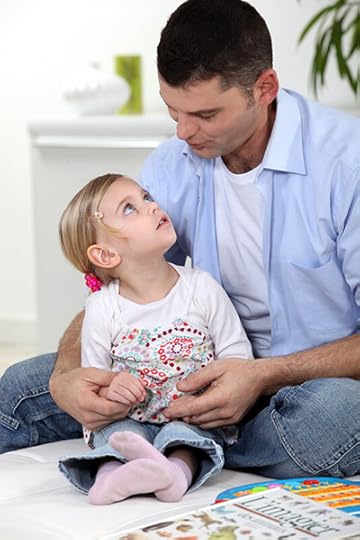 A father interacts with his daughter while looking at picture books. He makes the shape of a word with his mouth as she watches him. Making time to read together is important for child development.