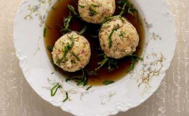 A bowl with three canederli dumplings in broth.