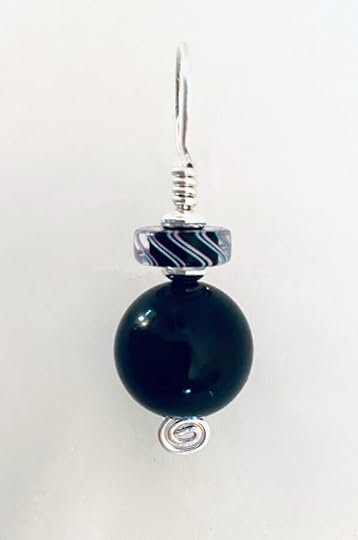 An elegant almost monochromatic pendant sharply contrasts against the plain white background. Silver wire is wrapped to form the pendant's head, with a spiral at the bottom. A disc with a black centre and tracing curves of pale blue and pink is mounted above a larger round black bead that gleams in the light.