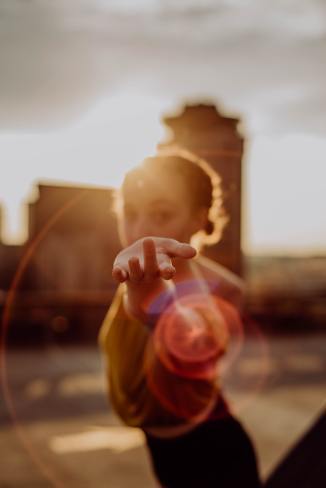 Image of a woman with light brown skin and hair pulled back in a tight bun standing with her hand outstretched to the camera in a dancer's pose. Focus is on her hand. Photo by Olivia Bauso on Unsplash.