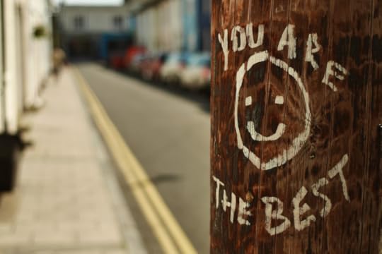 Image: an urban telephone pole on which someone has painted a smiley face and the words 