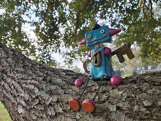 A small blue and pink robot sitting on a tree branch. The robot has a keyhole in its chest and an antique key strapped to its back.