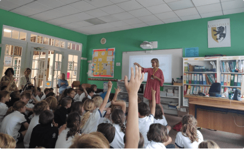 Classroom with pupils with hands up. Karen Inglis children's author at front of class