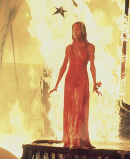 A blood-covered prom queen stand in front of a blazing fire