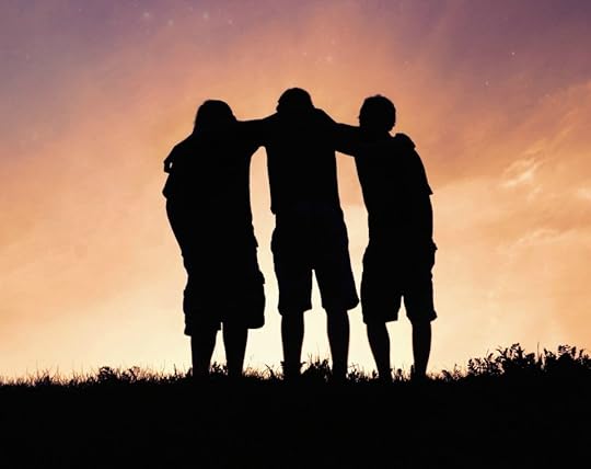 Silhouettes of three friends standing together and looking at a sunset.