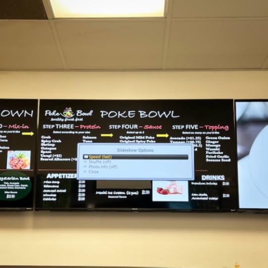 This is a photo of a large TV screen in the mall food court showing the menu for poke. On top of there menu for poke is the computer's equivalent of a menu: a list of 