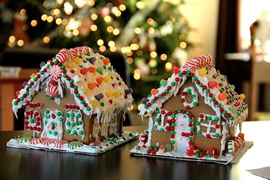 Two gingerbread houses covered in sweets and icing with a Yule tree lit up with fairy lights in the background