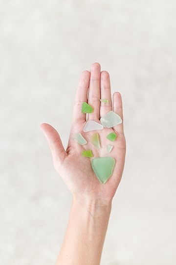 An extended hand with bits of water-smoothed green and clear glass on the palm