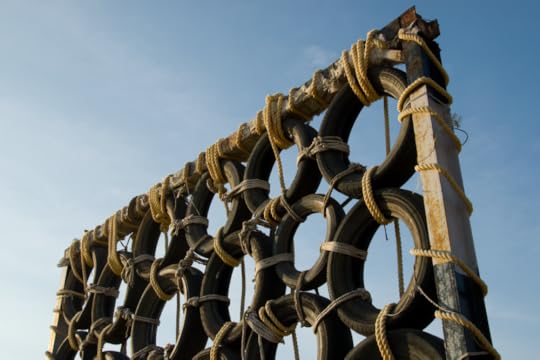 Image: as part of an obstacle course, automobile tires are tied together with rope and mounted in a tall metal frame that looms against a blue sky.